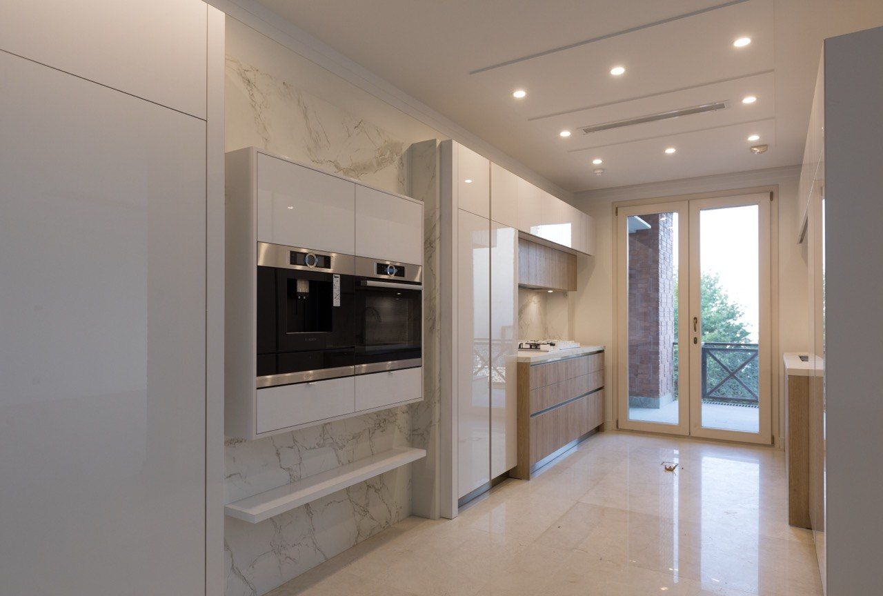 Bright galley kitchen with white cabinetry, built-in ovens and stone floors